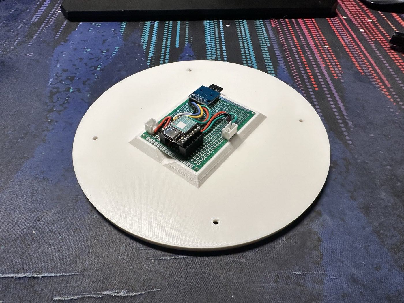 A green perfboard carrying a small microcontroller and a microSD module, mounted on a printed riser on the white base plate