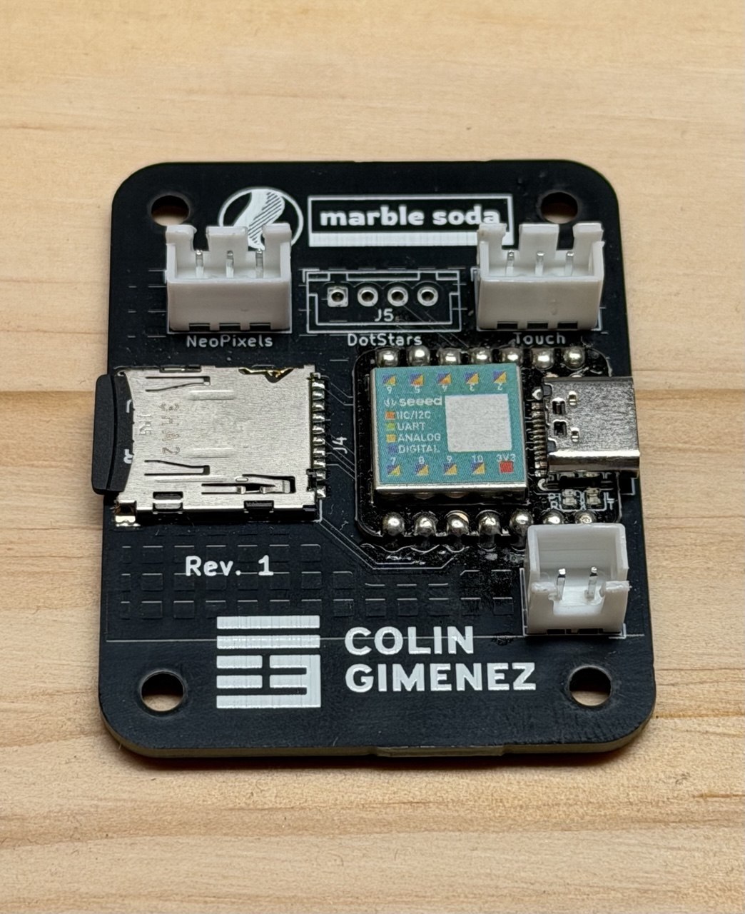 A black custom PCB labeled marble soda and Colin Gimenez, with a microSD slot, a Seeed microcontroller, and JST connectors for NeoPixels, DotStars and Touch